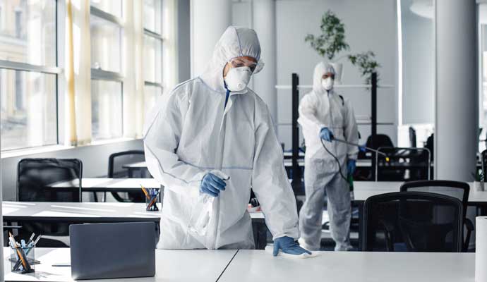 Professional office disinfection service by trained experts Two experts in protective suits disinfecting office desks and surfaces using spray bottles and cleaning equipment