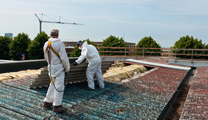 Two people are removing asbestos from house roof Two people are removing asbestos from house roof
