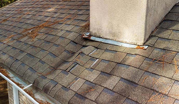 Roof with damaged shingles and debris around a chimney