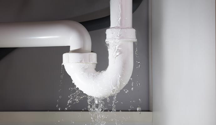 A leaking white PVC pipe under a sink